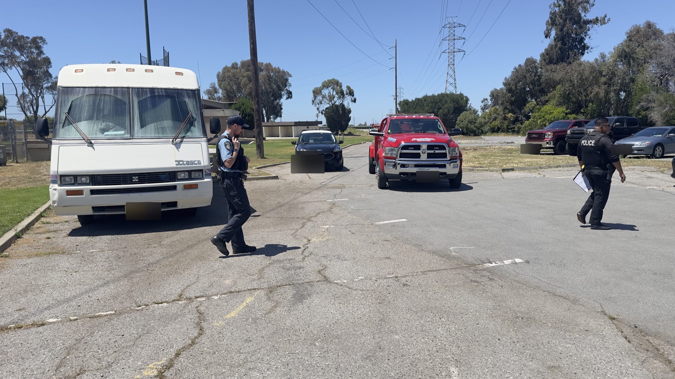 Wide view of an RV, officer, and tow truck in a parking lot on June 1, 2026
